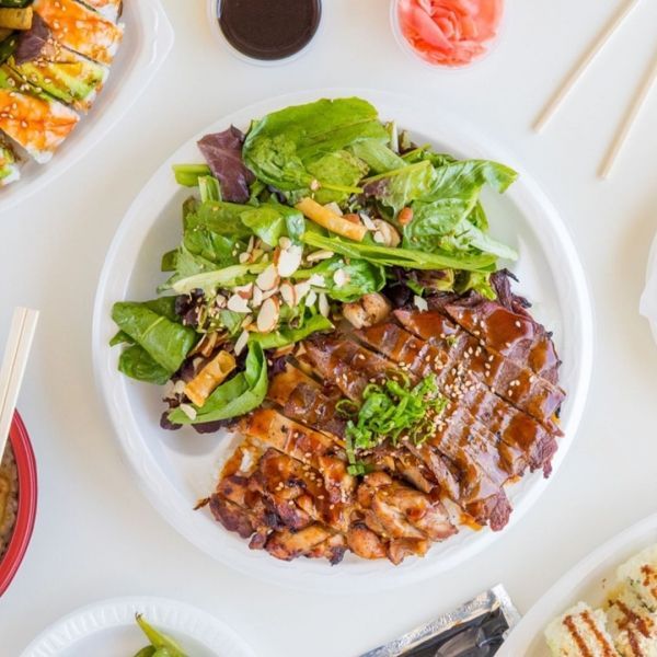 Chicken teriyaki with salad on a white plate, sushi in the background.