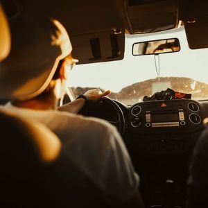 Person driving a car, hands on the steering wheel, bright sunlight. Interior view.