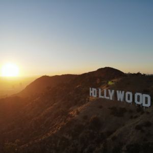 Sunset over the Hollywood sign on a hillside. The sky is orange and blue.