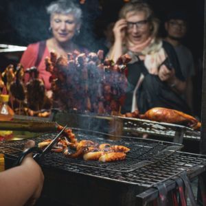 Street food vendor grilling food. Customers watch; smoke rises.