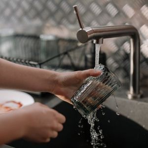 Person washing a glass under running water in a stainless steel sink.
