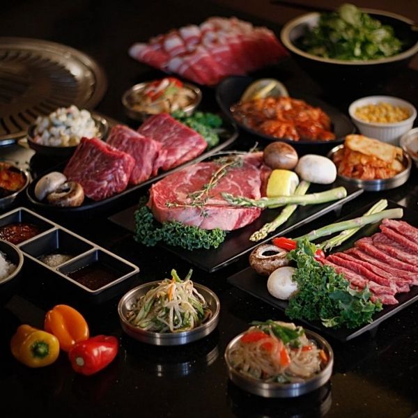 Korean BBQ spread with raw meats, vegetables, and side dishes on a table.