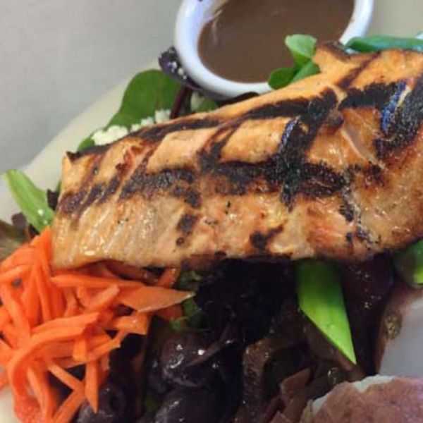 Grilled salmon fillet over salad with carrots and sauce.