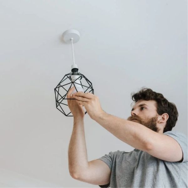 Man installing a pendant light fixture on a white ceiling.