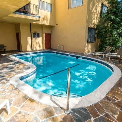 A small, kidney-shaped swimming pool in a courtyard, surrounded by beige and brown stone.