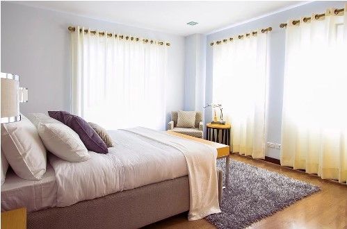 Bedroom with white walls, large bed, sheer curtains, armchair, and rug.