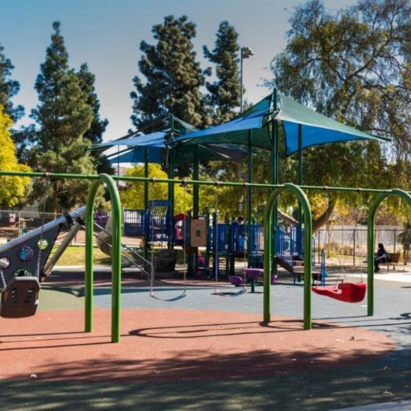 Playground with swings, slides, and climbing structures under shade, sunny day.