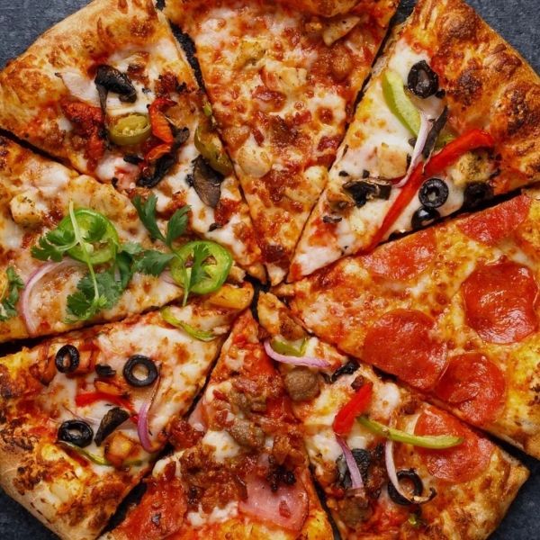 Pizza cut into eight slices, with various toppings, including peppers, olives, and pepperoni.