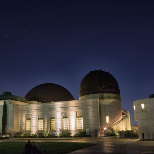 Griffith Observatory at night, lit beige building with dark domes under a deep blue sky.