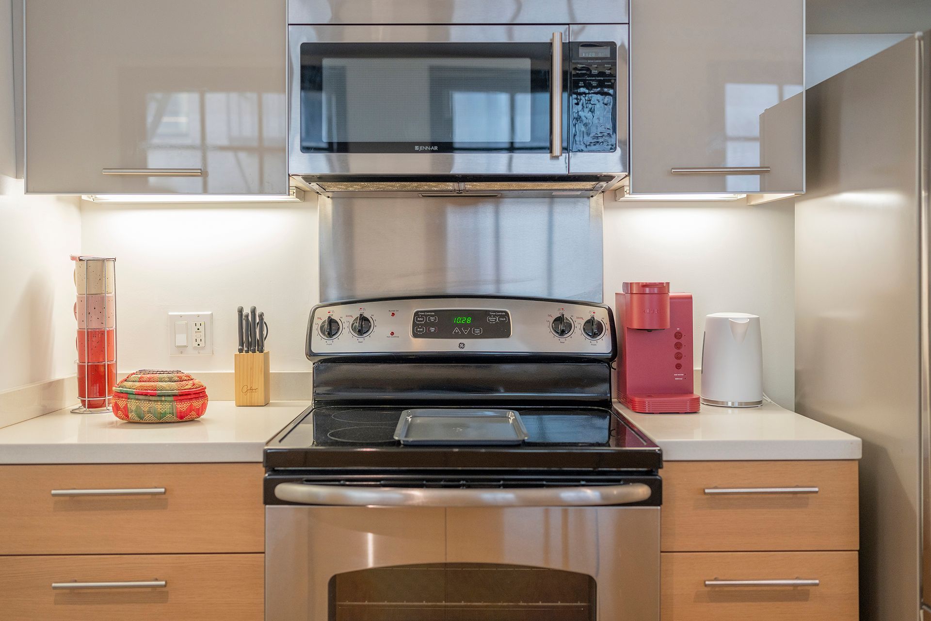 Modern kitchen with stainless steel appliances, light wood cabinets, and white countertops.