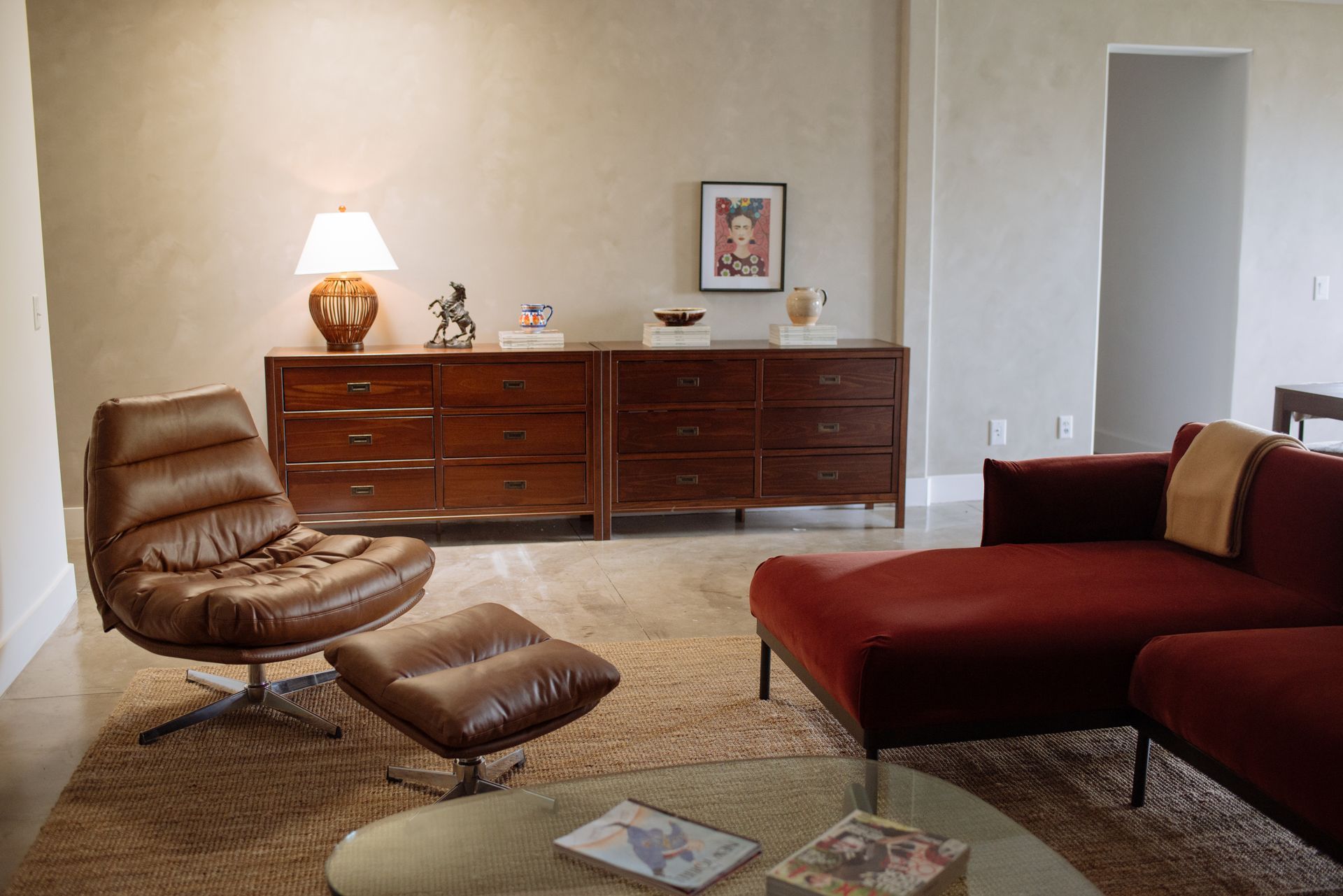 Living room with brown leather chair and ottoman, red couch, and wood dressers.