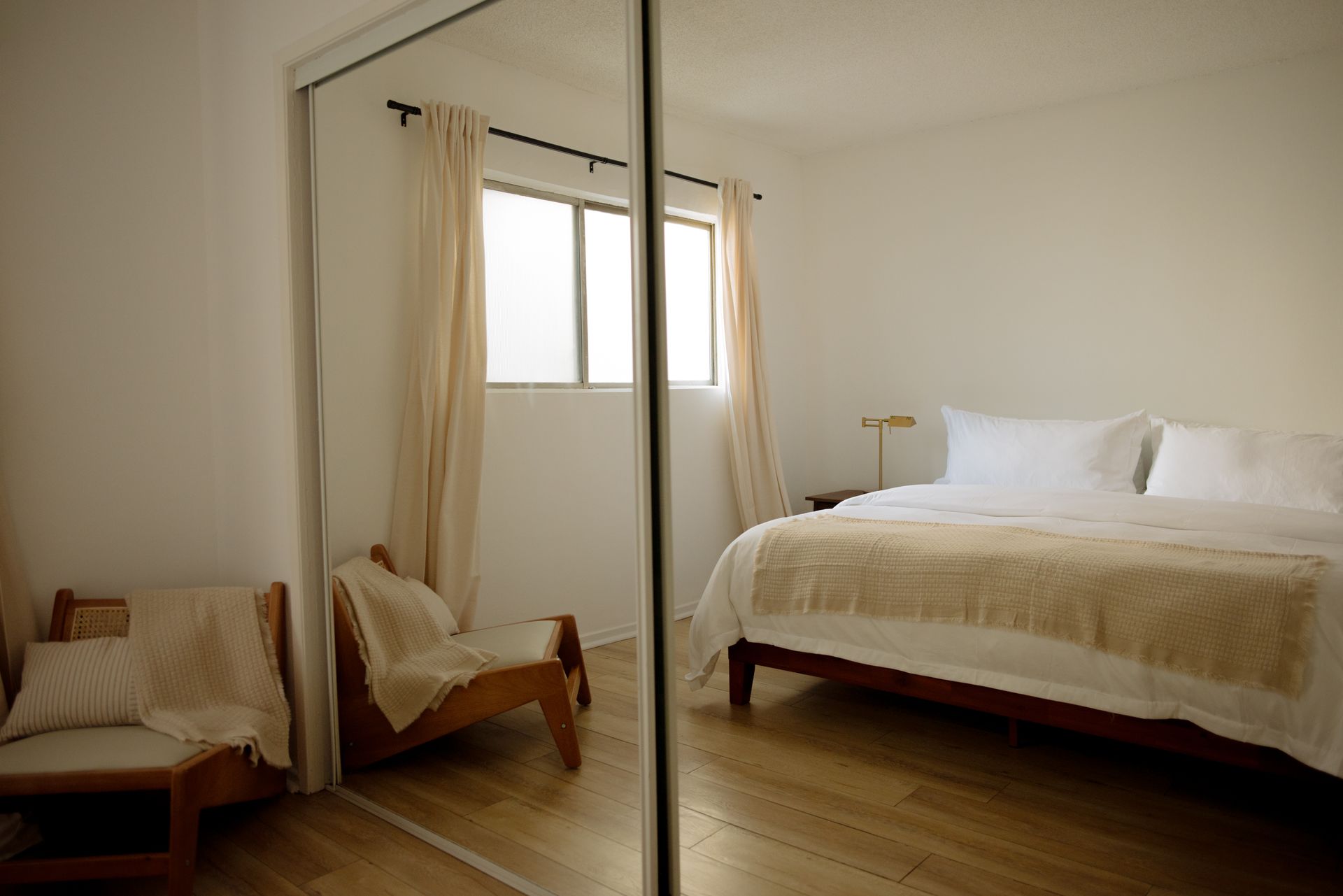 Bedroom with mirrored closet doors reflecting the bed, chairs, and window with curtains.