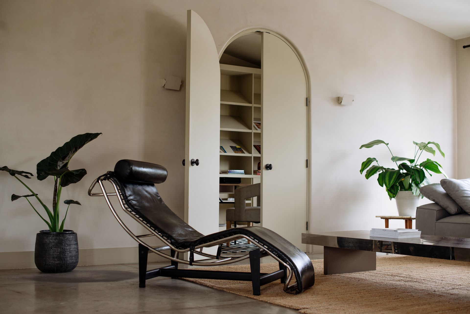 Living room with leather chaise lounge, arched doorway, and potted plants.