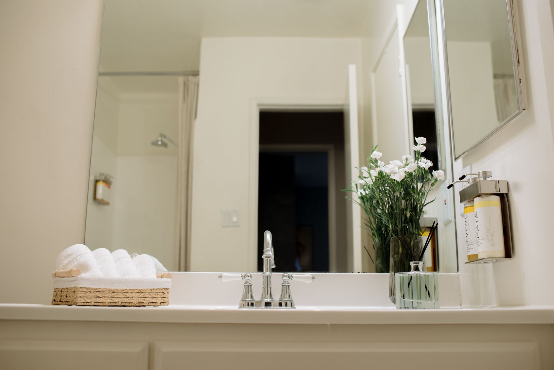 Bathroom sink area with mirror, flowers, and basket of towels.