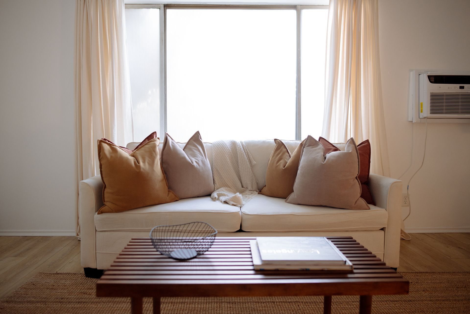 Living room with a white couch, pillows, wooden coffee table, and large window.