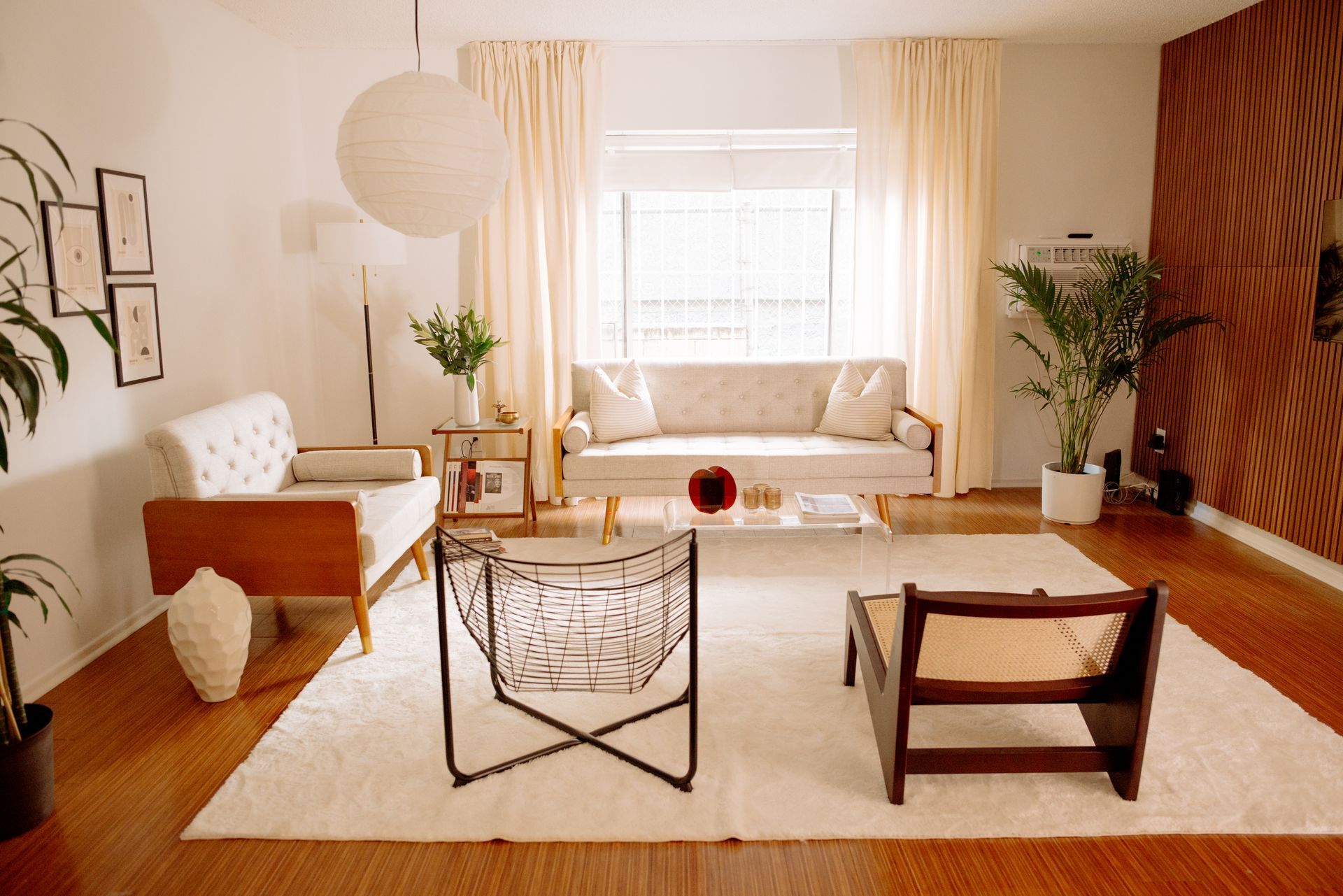 Living room with white walls, ivory curtains, light-colored furniture, and large rug.