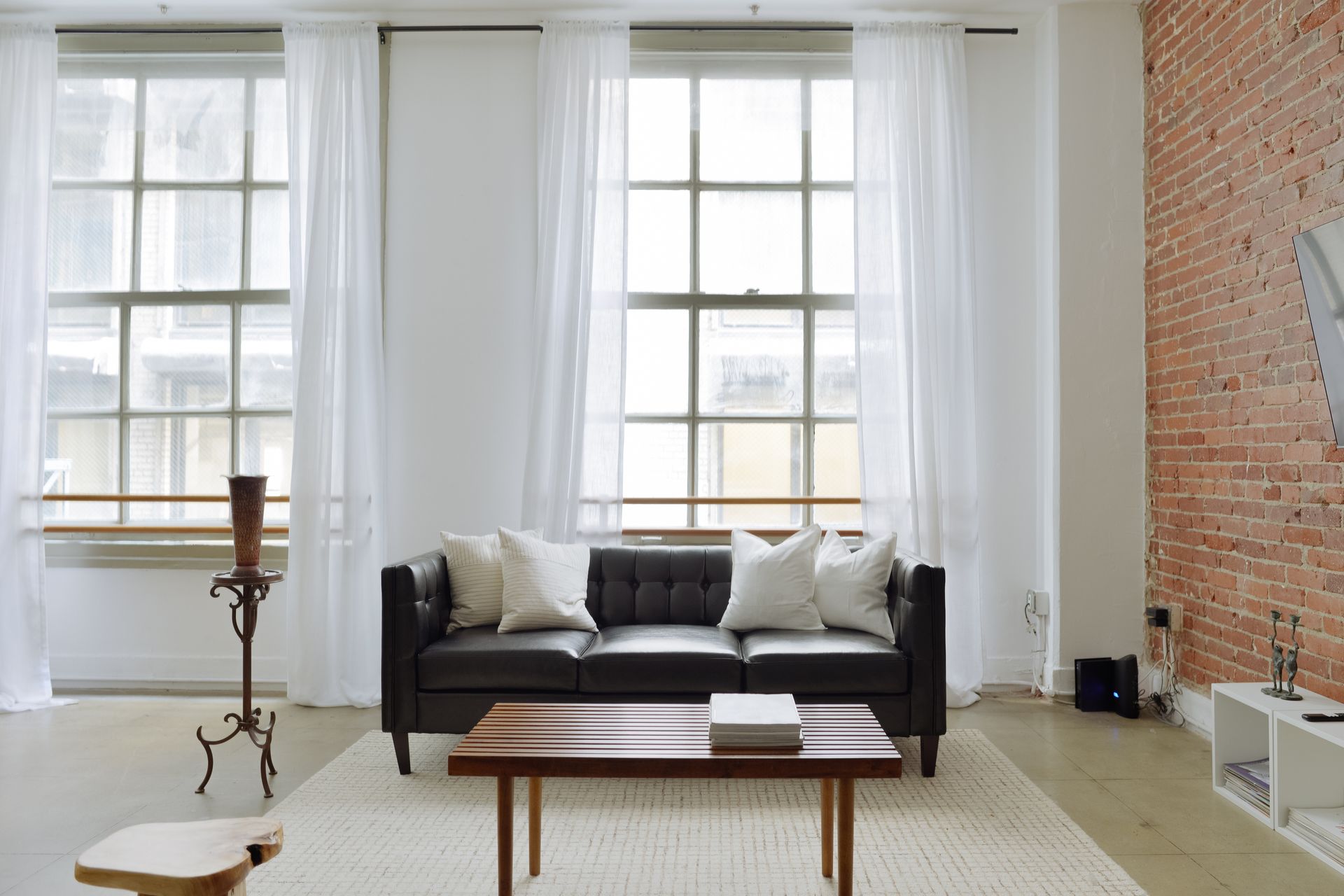 Living room with black sofa, wood coffee table, sheer white curtains, and exposed brick wall.