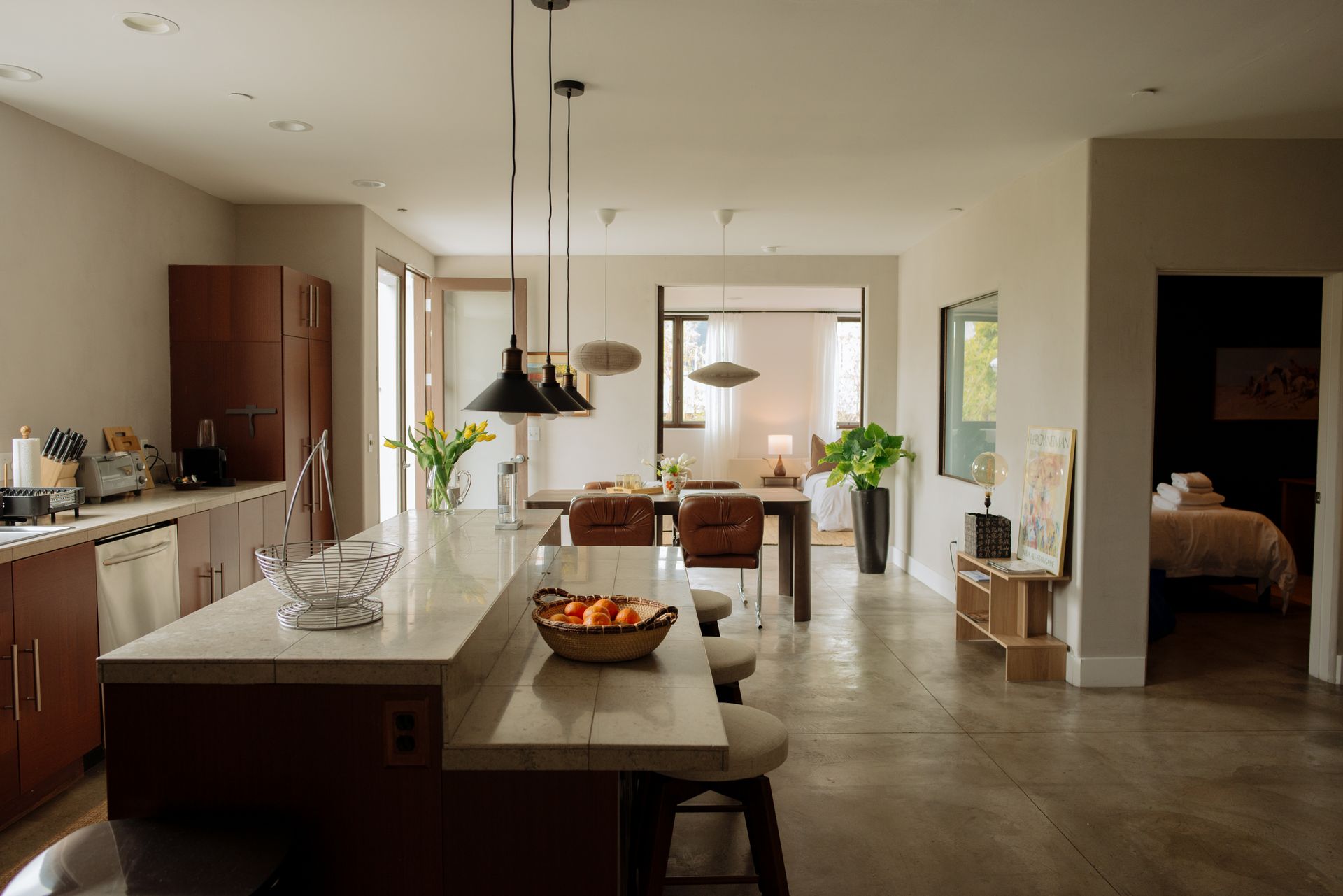 Modern kitchen and dining area with a kitchen island, table, and bedroom in the background.