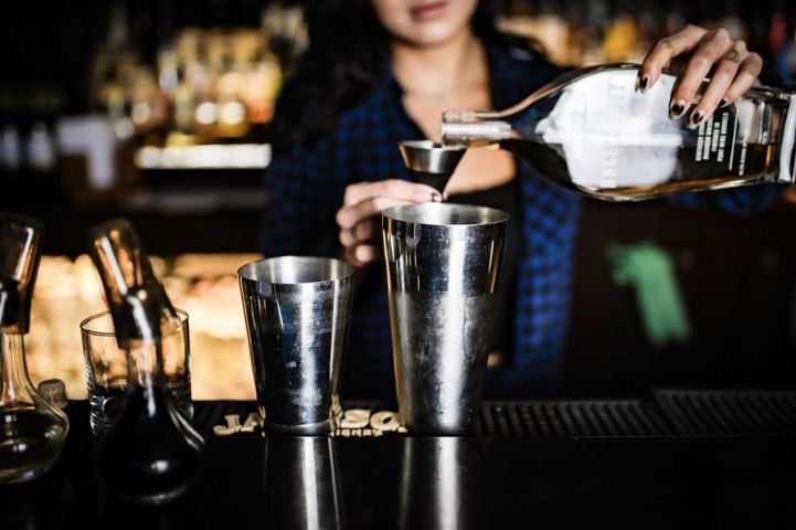 Bartender pouring drink into shaker at bar.