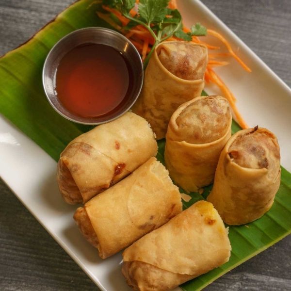 Egg rolls with dipping sauce on a white plate with a banana leaf.