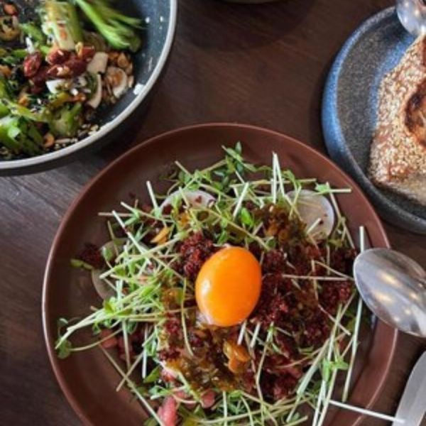 Overhead view of a salad with sprouts, egg yolk, and sun-dried tomatoes on a brown plate, with other dishes nearby.