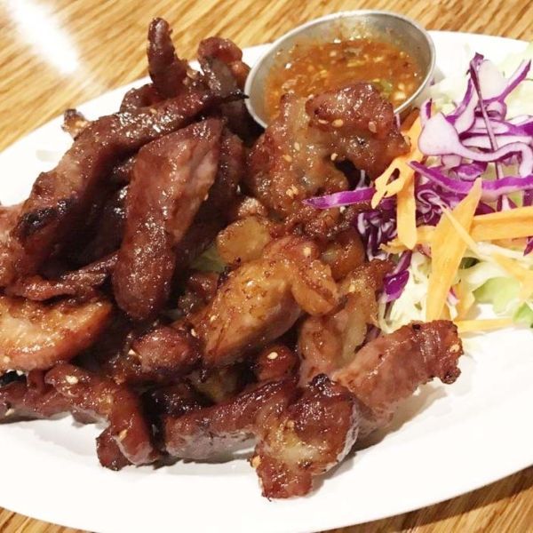Plate of grilled pork with sauce and shredded vegetables.