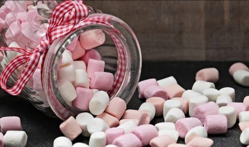 Jar of marshmallows, pink and white, spilling onto a dark surface, tied with red and white ribbon.