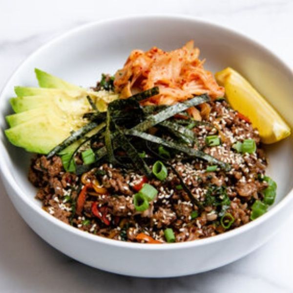 Beef bowl with kimchi, avocado, and seaweed in a white bowl.