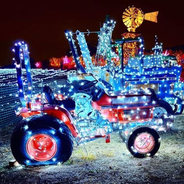 Tractor decorated with blue and white Christmas lights, red wheels, and a windmill against a dark night sky.