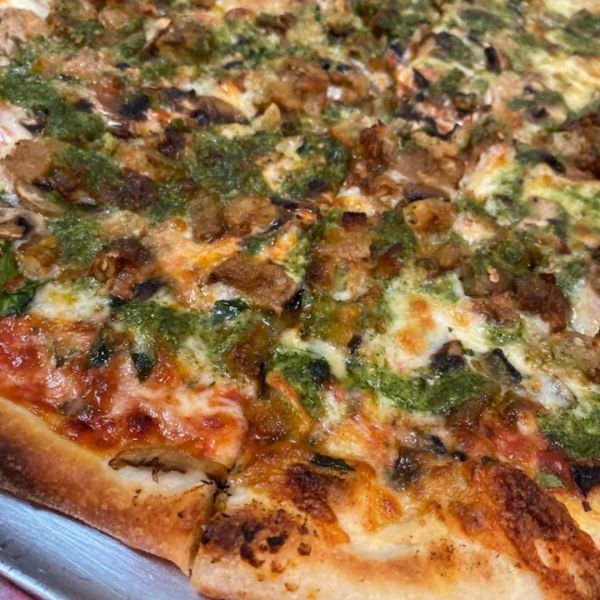 Pizza topped with green pesto, mushrooms, and sausage.
