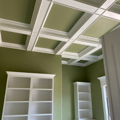 A room with green walls and white shelves and a coffered ceiling
