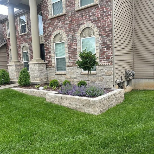 Brick house with a stone planter filled with lavender and small shrubs. Green lawn in the foreground.