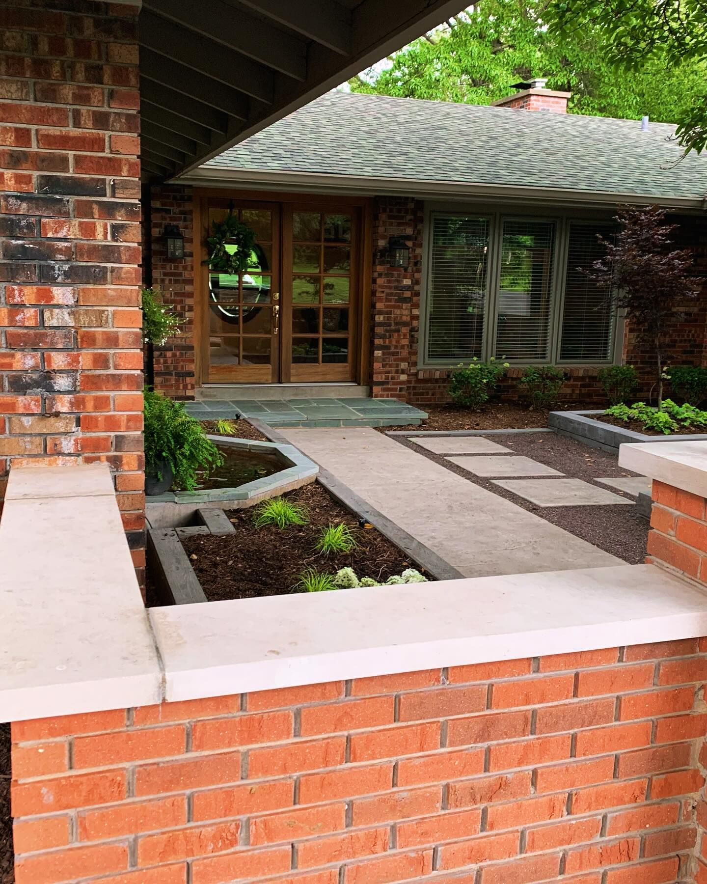 Brick facade of a house with a concrete walkway and landscaped beds leading to a front door.