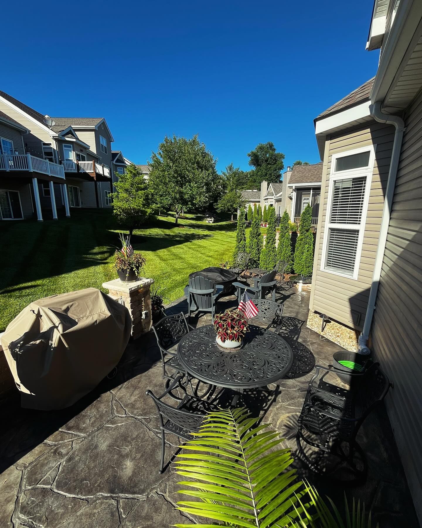 Patio with wrought iron furniture, green lawn, clear blue sky, and surrounding houses.