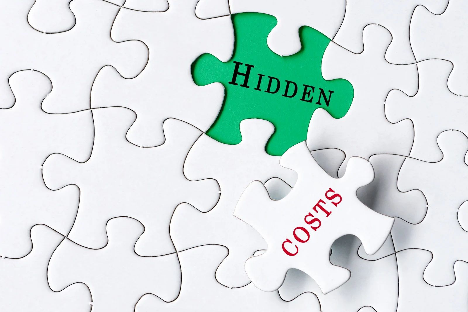Puzzle pieces with green “HIDDEN” piece and white “COSTS” piece on a white background