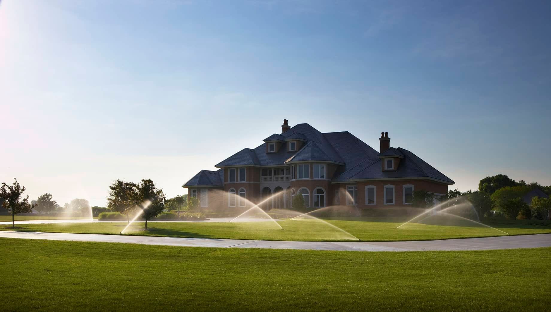 A large house with sprinklers spraying water on the lawn in front of it.