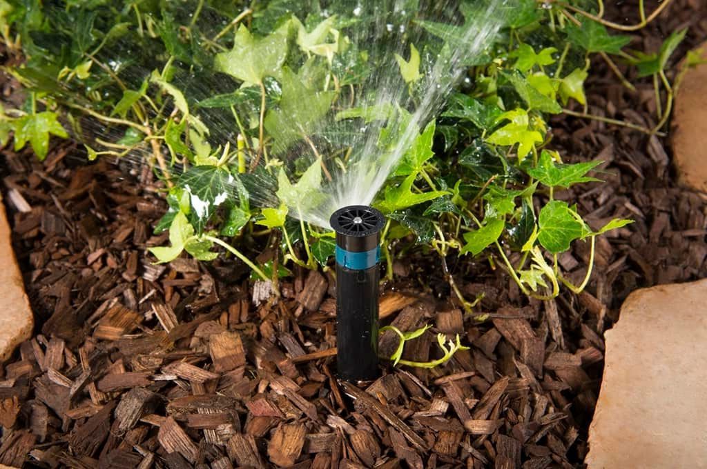 A sprinkler is spraying water on a pile of mulch in a garden.