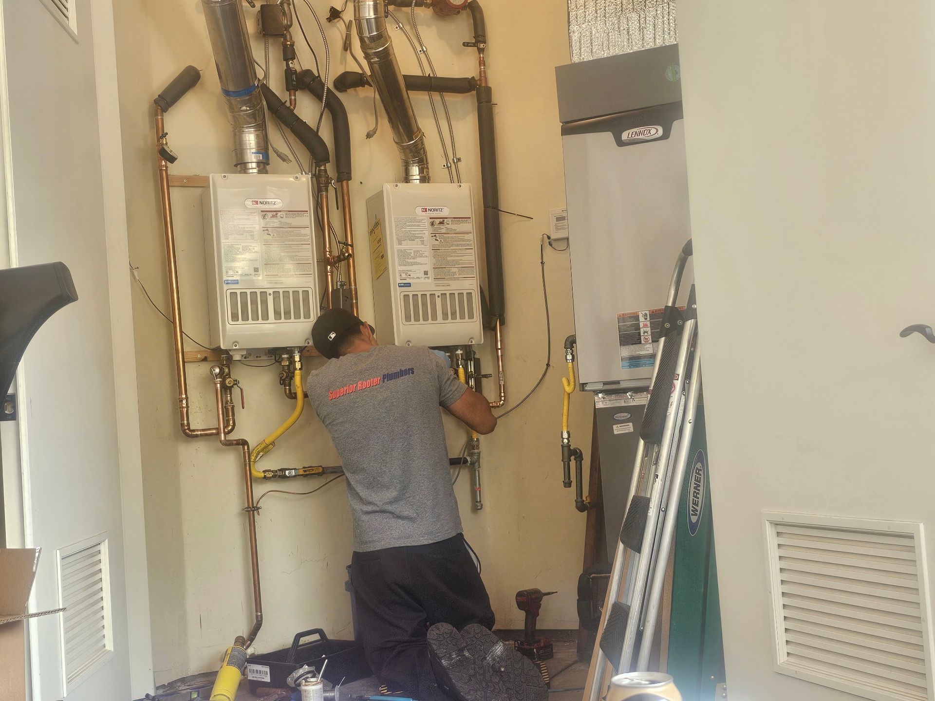 Technician inspecting and repairing HVAC units in a utility closet, with exposed pipes and wiring.