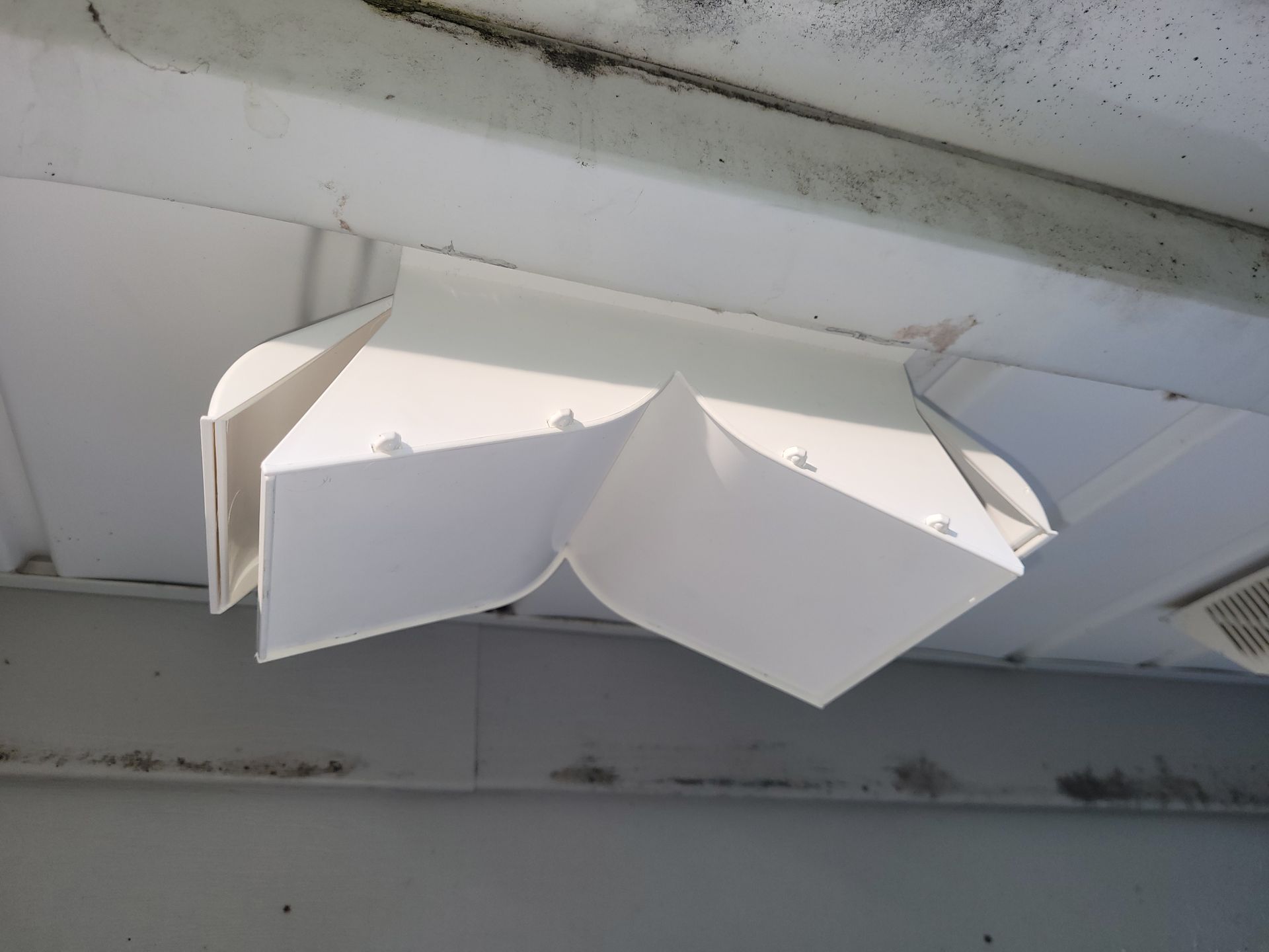 White plastic vent attached to a white ceiling, with a weathered appearance.