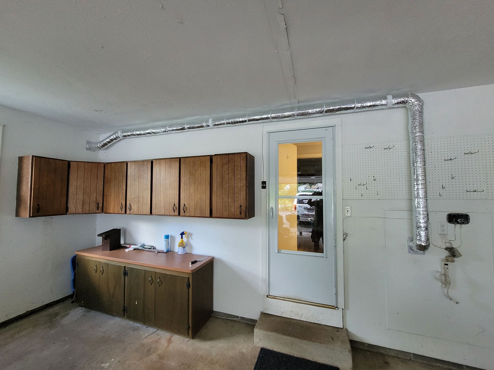 Garage interior with cabinets, a door, and a silver vent pipe along the ceiling and wall.