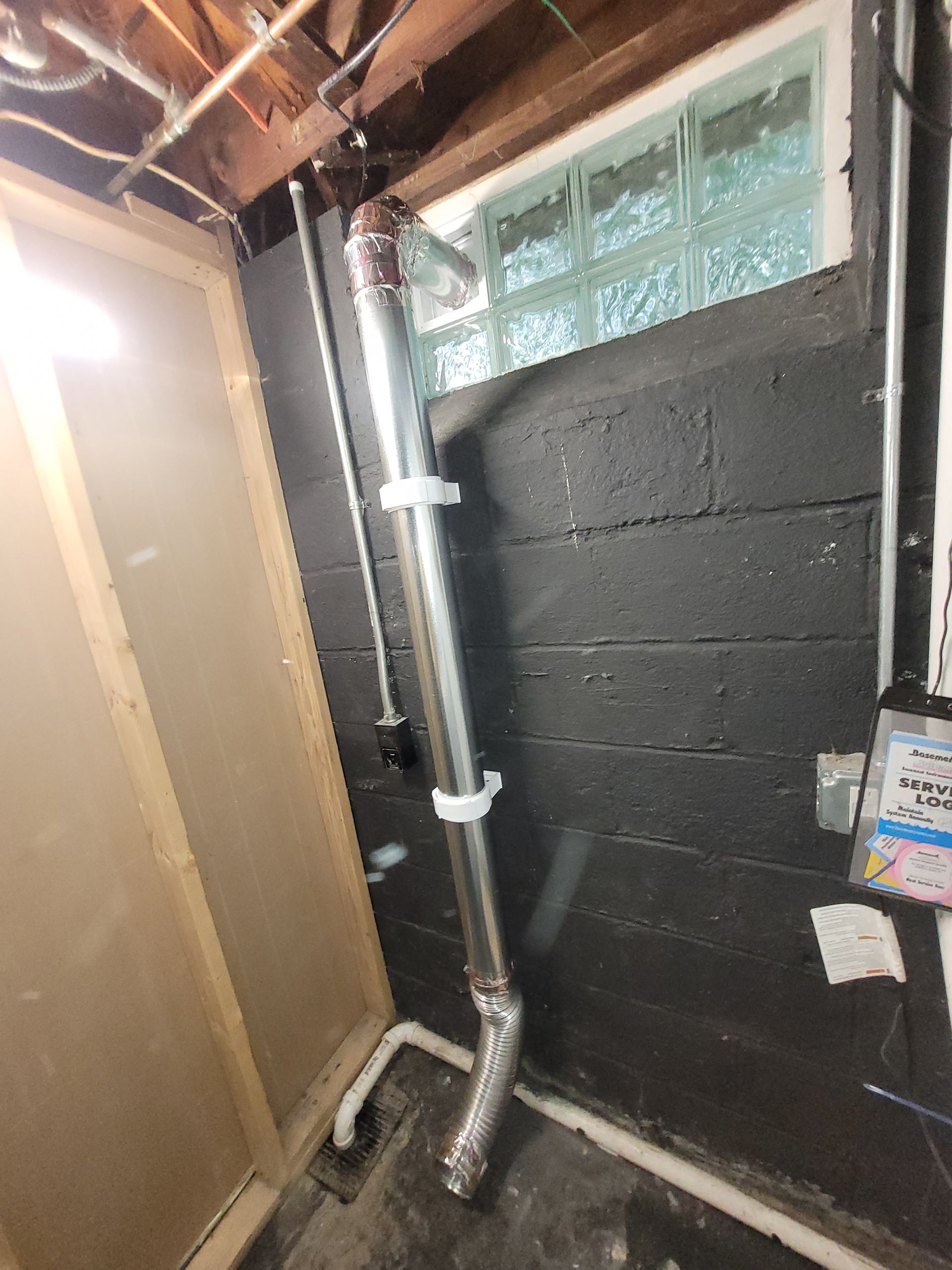 A metal pipe runs vertically along a black cinderblock wall with a window.