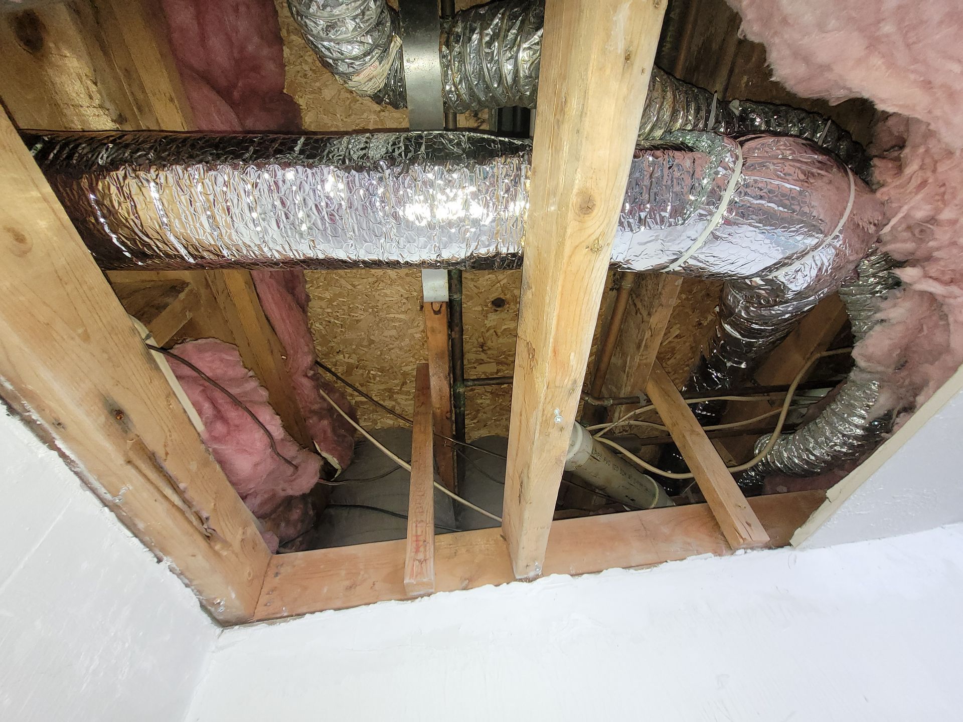 Looking up at exposed ceiling framing with ductwork and insulation.