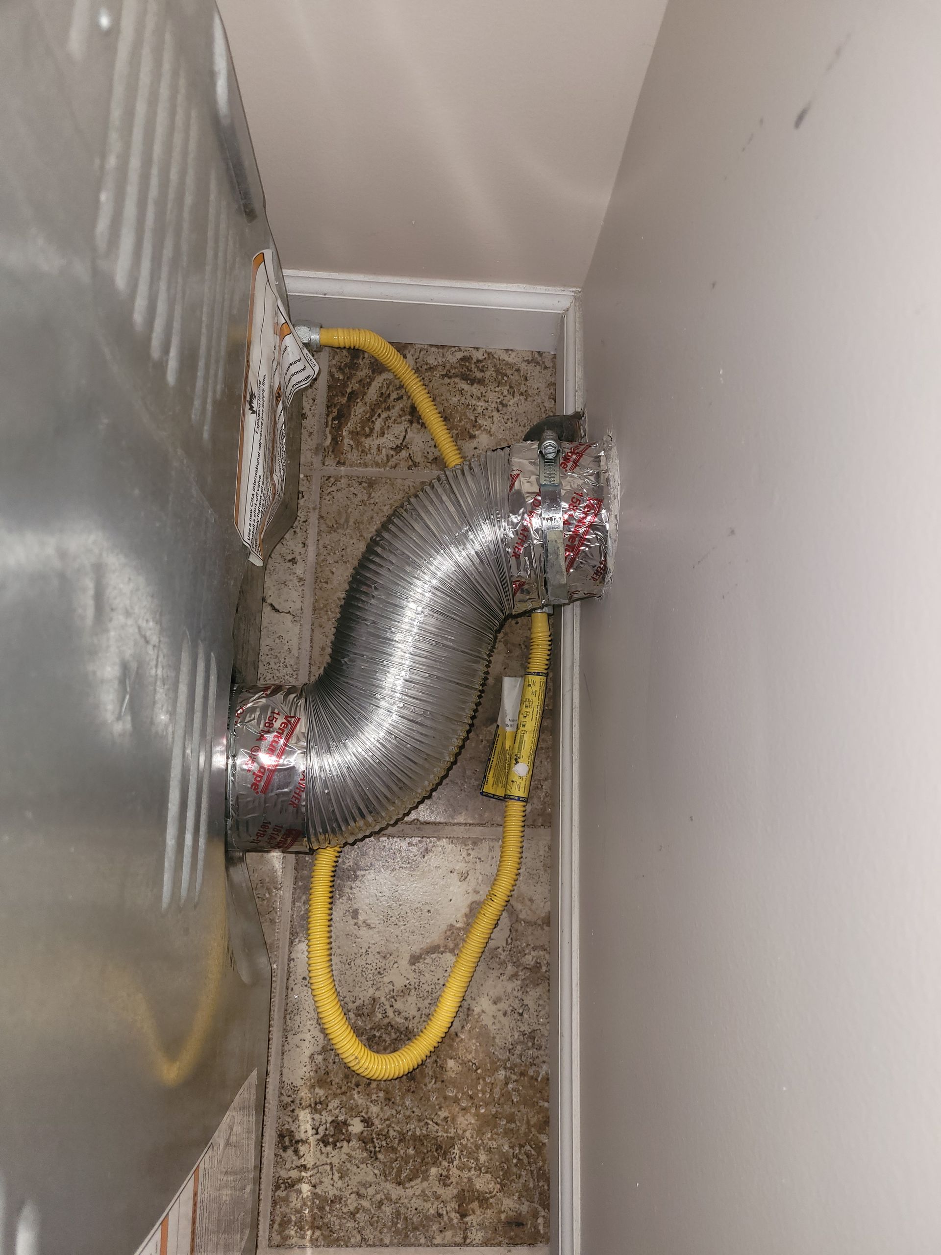 A dryer vent connected to a wall with a flexible silver tube.