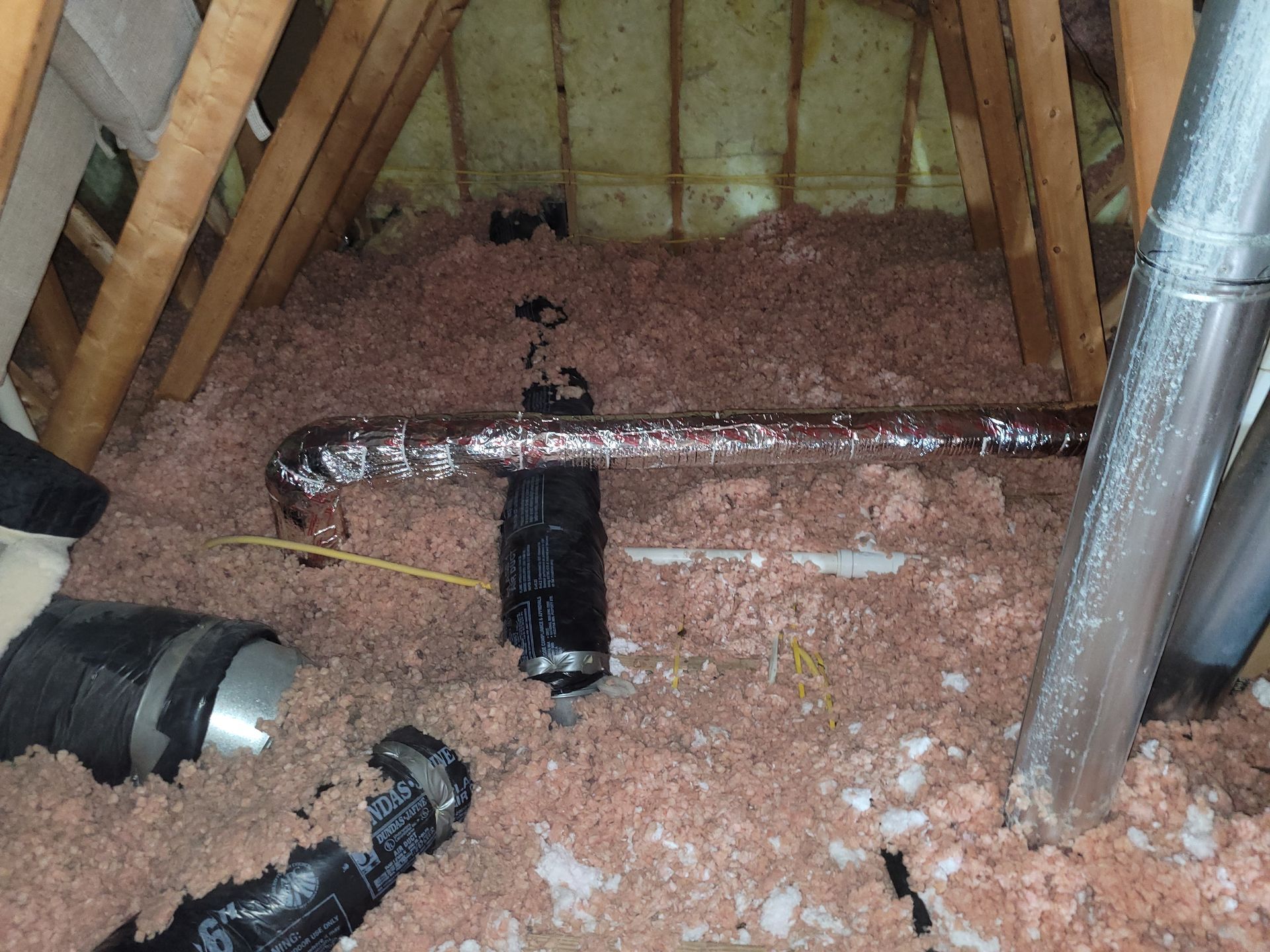 Attic space with pink insulation, ductwork, and wooden rafters.