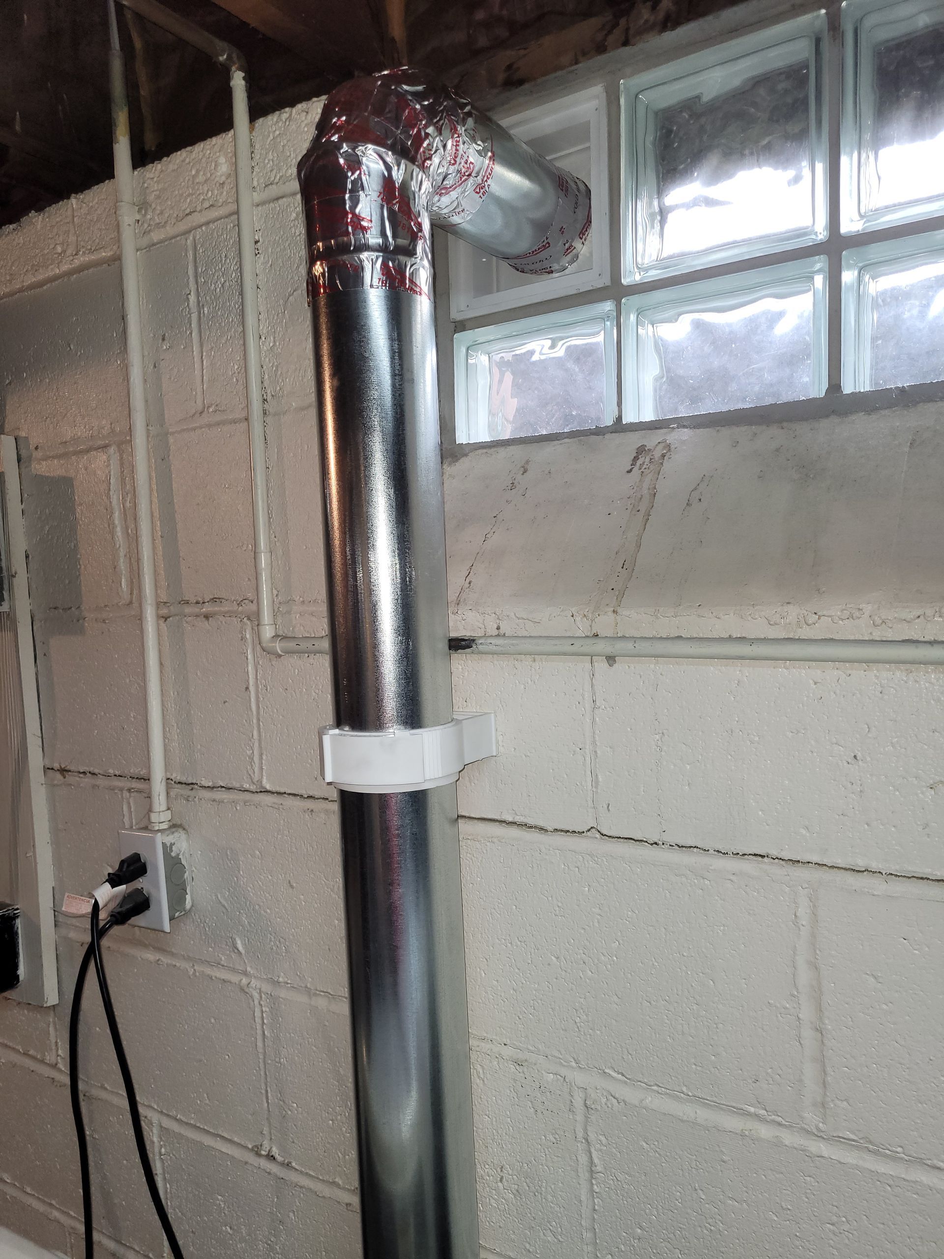 Metal dryer vent pipe angled upwards, running near a window.