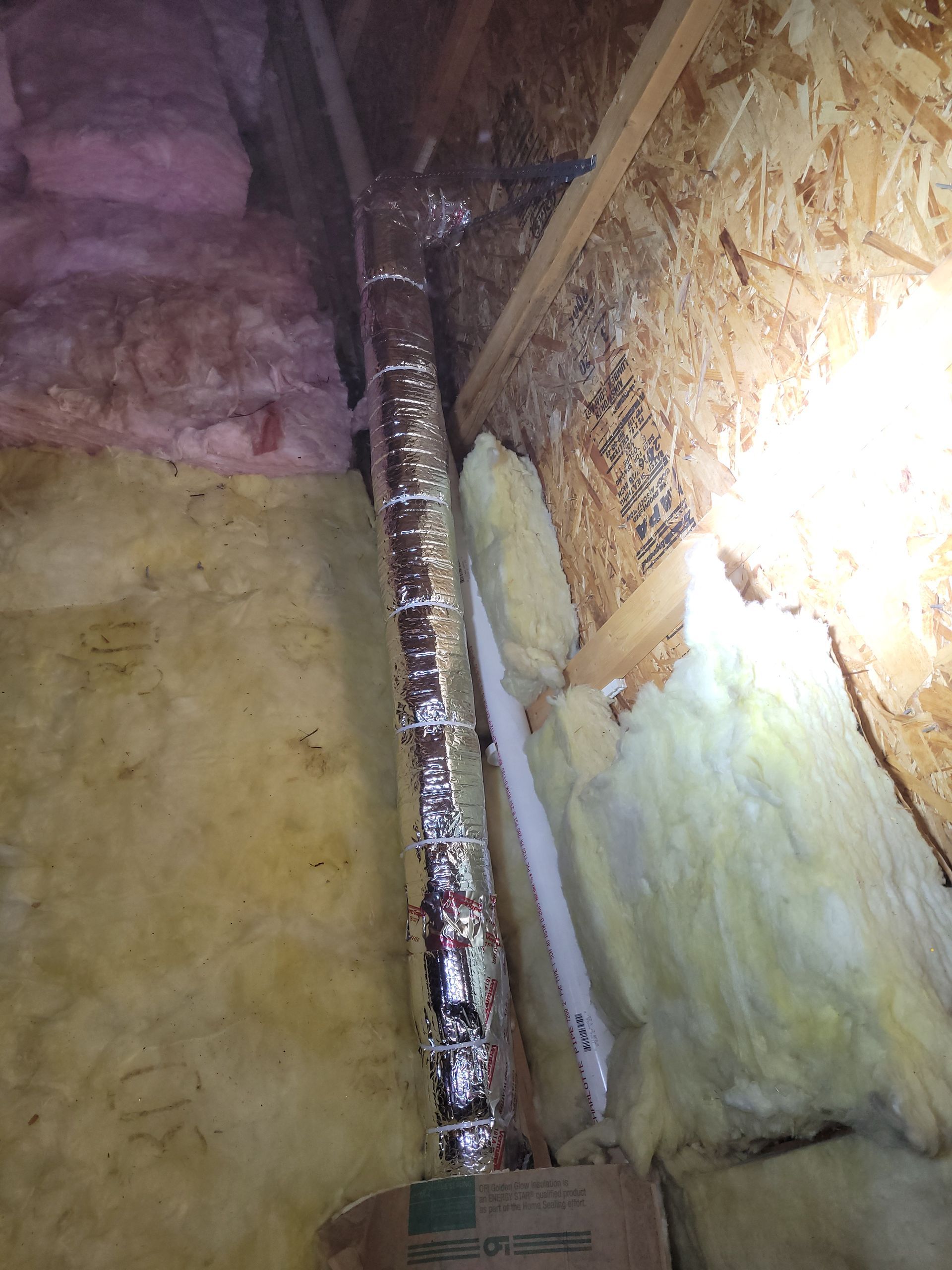 Attic view with silver ductwork and insulation, and exposed wood.