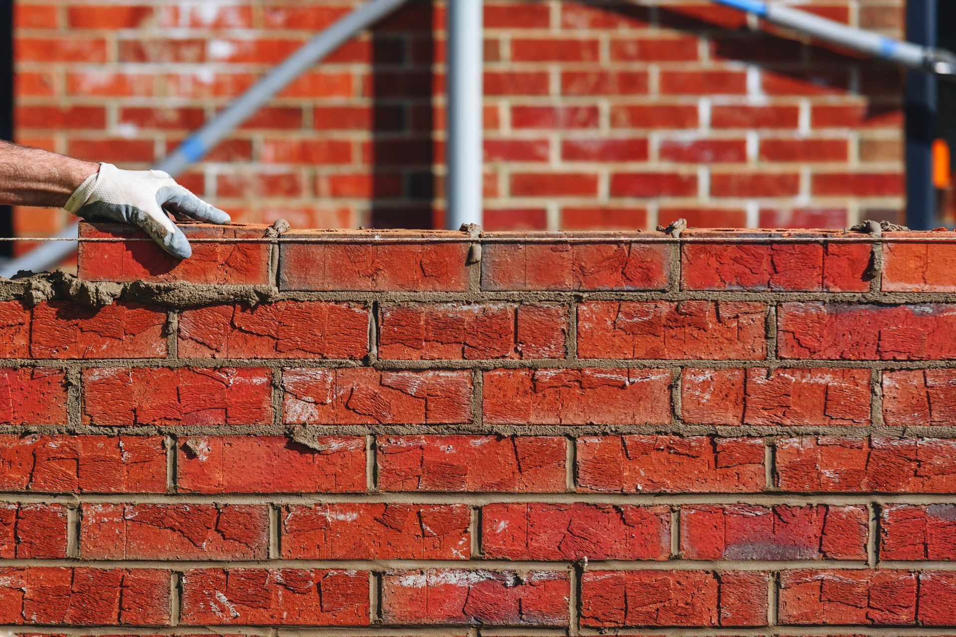 Gloved hand applying mortar on a red brick wall during construction.