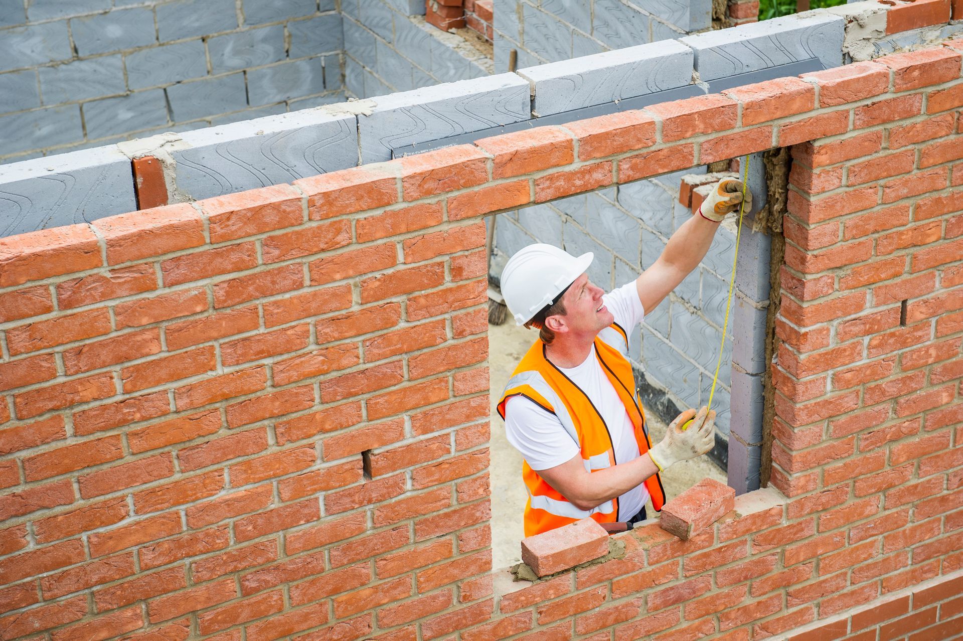 A worker is using a measuring tape to lay some bricks. A worker is using a measuring tape to lay some bricks.