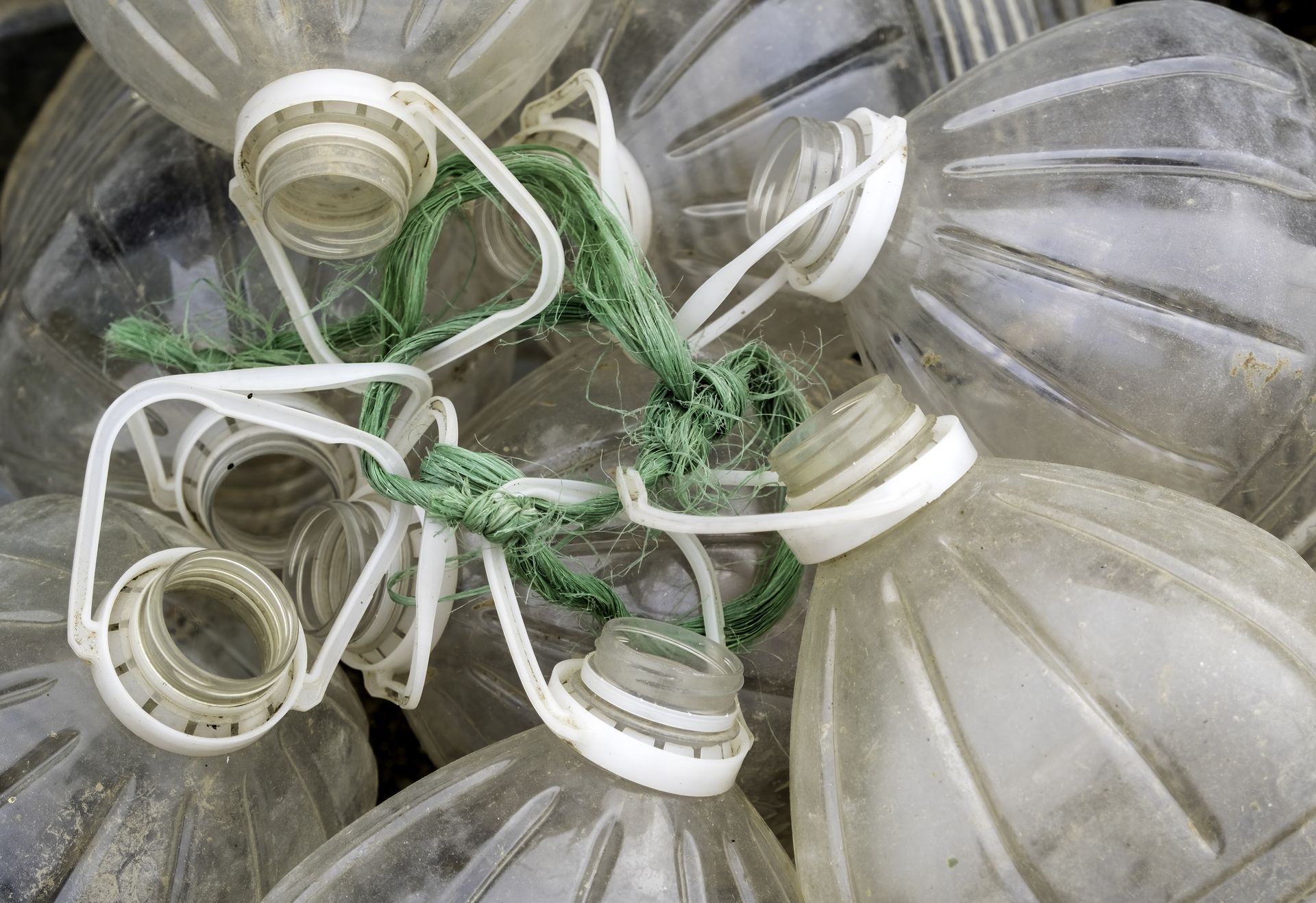 Close-up of clear plastic bottles with white caps and green rope tied together.