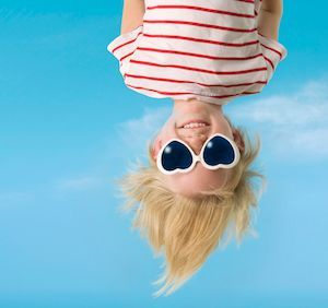 A person wearing heart-shaped sunglasses and a striped shirt, pictured upside down against a clear blue sky.